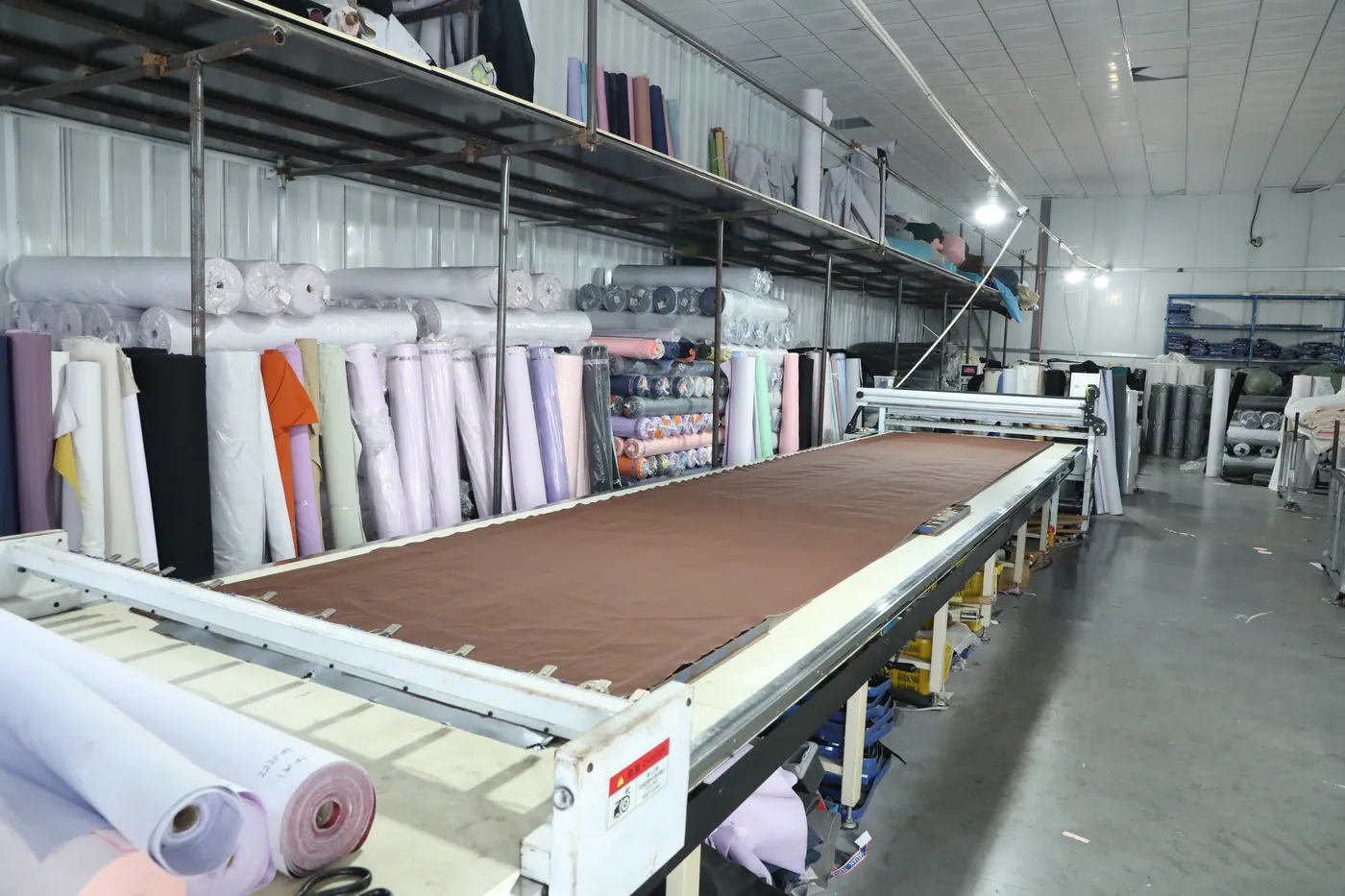 CNC cutter slicing through a multi-layer spread of pink backpack fabric