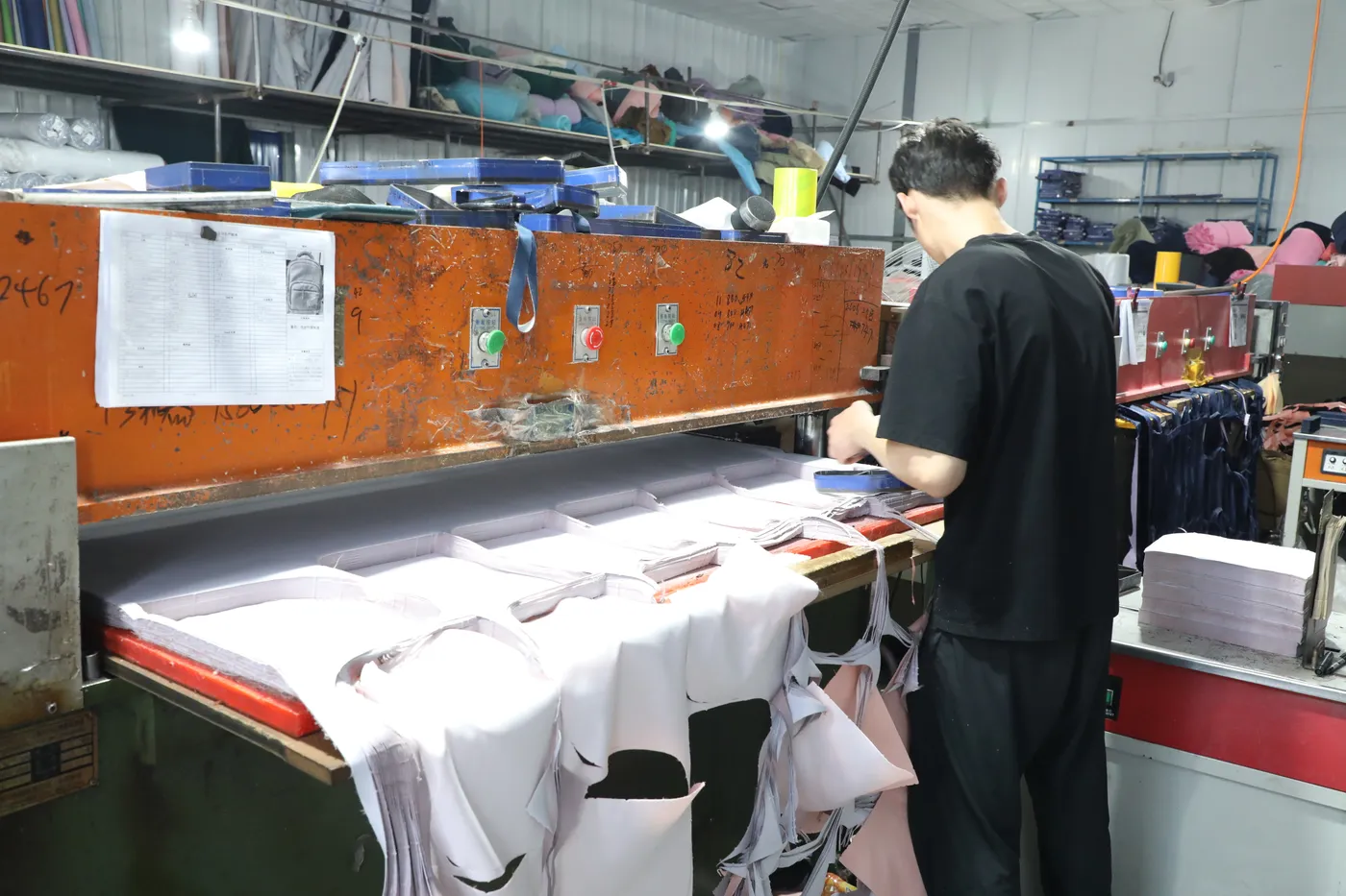 Operator working a hydraulic die-cutting press on cut backpack components